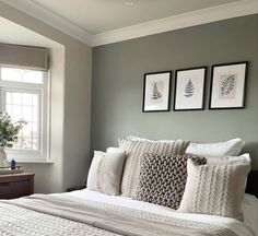 a bed with white sheets and pillows in a bedroom next to two framed pictures on the wall