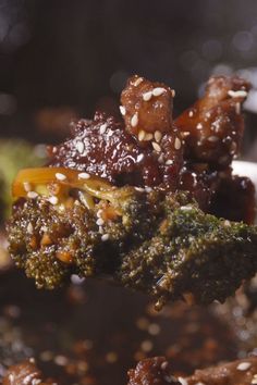 broccoli and other food is being held up by a spoon with sesame seeds on it