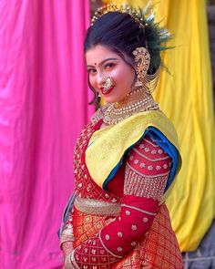 a woman in a red and yellow dress with gold jewelry on her head, standing next to colorful cloths