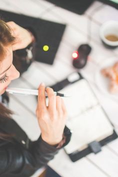 a woman sitting at a table with a pen in her hand and writing on it