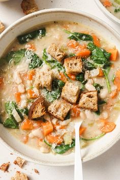 two bowls filled with soup and croutons on top of a white tablecloth