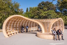 two people sitting on benches in the middle of a park with an open wooden structure