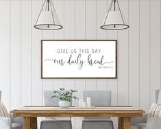 a dining room table with chairs and a framed sign above it that says give us this day our daily bread