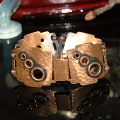 two metal bracelets sitting on top of a black table next to a glass vase