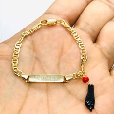 a hand holding a gold chain bracelet with a black and red bead on it