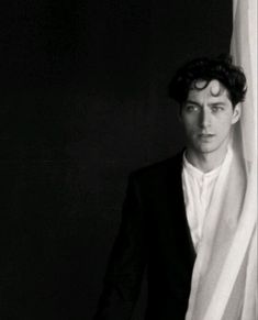 black and white photograph of a young man in a tuxedo leaning against a curtain