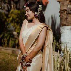 a woman in a white and gold sari is standing by some palm trees with her hand on her hip