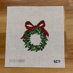 a cross stitch christmas ornament with a red bow and holly wreath on it