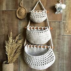 three crocheted baskets hanging on the wall next to a potted grass plant