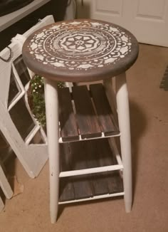 a wooden stool with an intricate design painted on the top and bottom, sitting in front of a door