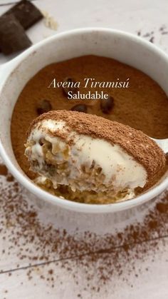 a bowl filled with pudding and ice cream on top of a white table next to a spoon