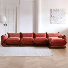 a red couch sitting on top of a wooden floor next to a white rug in a living room