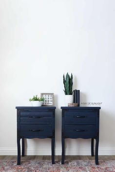 two dark blue nightstands with plants on top of them in front of a white wall