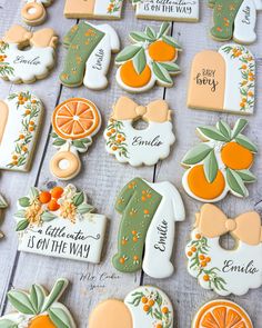 decorated cookies with oranges and green leaves are arranged on a wooden surface, along with the words baby is on the way