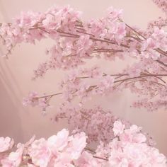 some pink flowers are in a vase on a table and the wall is painted white