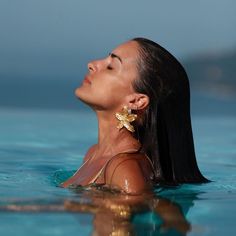 a woman is floating in the water with her eyes closed and ear rings dangling from her ears