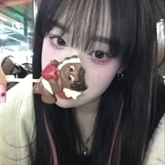 a girl with long black hair eating a piece of cake in front of her face