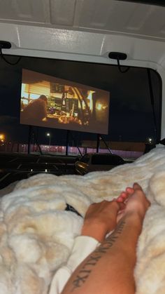 a person laying in bed with their feet up on the blanket and watching a movie