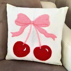 a white pillow with two cherries on it and a pink bow hanging from the back