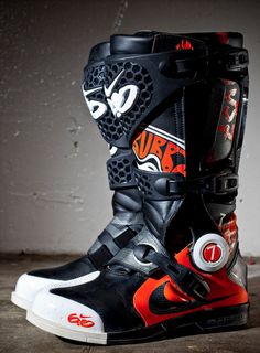 a pair of black and red motorcycle boots with white soles on concrete floor next to wall