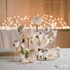 a table topped with lots of glass vases filled with white flowers and crystal goblets