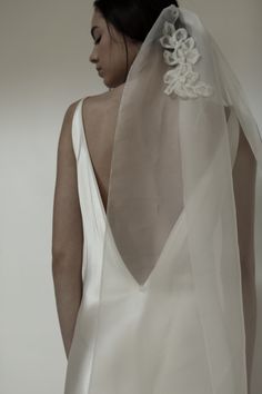 the back of a woman's wedding dress with a veil over her head and flowers on it