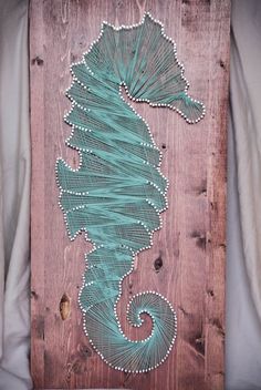 a wooden sign with a seahorse painted on it's side and string wrapped around the bottom