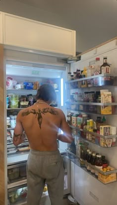 a man standing in front of an open refrigerator with his back turned to the camera