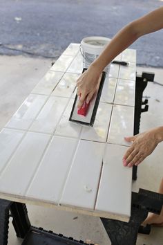 a woman is using a sponge to clean the tile on top of a white table