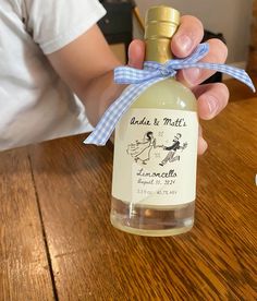 a person holding a bottle of wine on top of a wooden table with a ribbon around it