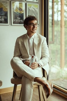 a man sitting in a chair holding a drink and smiling at the camera with posters on the wall behind him