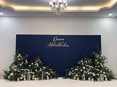 a blue backdrop with white flowers and greenery on the bottom is surrounded by candles