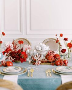 the table is set with plates, silverware and red flowers