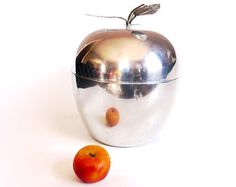 an apple and orange sitting next to each other on a white surface with a silver lid