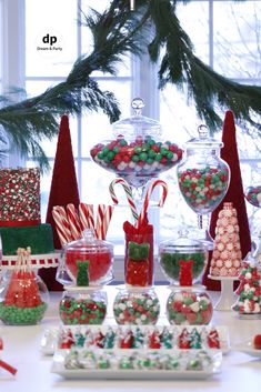 a table topped with lots of candy and candies next to a christmas tree in the background