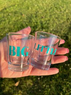 two shot glasses with the words big little on them are held in someone's hand