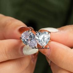 two heart shaped diamond studs being held by someone's hands with their fingers