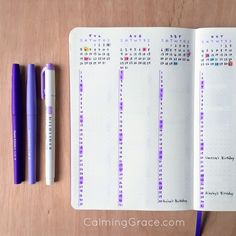 an open planner and two pens on a wooden table with the calendar written in purple