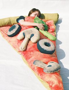 a woman laying on top of a slice of pizza shaped sleeping bag with stuffed animals