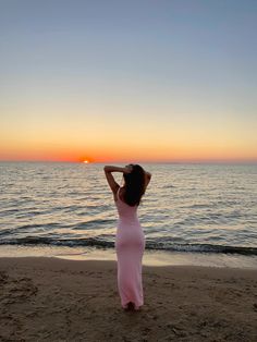 a woman standing on top of a sandy beach next to the ocean at sun set