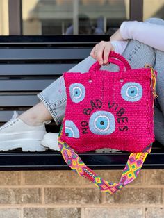 a woman sitting on a bench holding a pink purse with an evil eye drawn on it