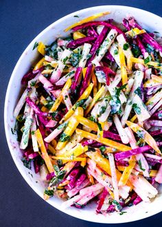 a white bowl filled with colorful vegetables on top of a blue tablecloth next to a fork