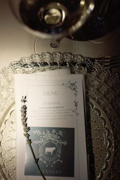 a menu on a glass plate with a wine glass in the backgrouf