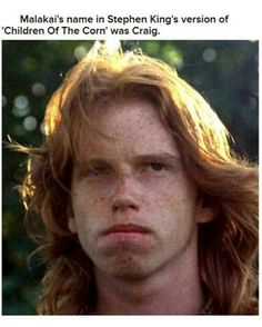 a young man with freckled hair stares into the distance while standing in front of trees