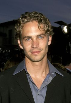 a man with curly hair and blue eyes smiling at the camera while standing in front of a crowd