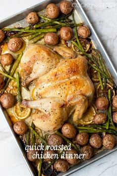 a roasted chicken with asparagus and potatoes in a baking pan on a marble countertop