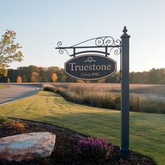 a sign that says true stone on it in front of some grass and flowers near a road