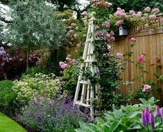 a garden with lots of flowers next to a wooden fence and some plants growing on it