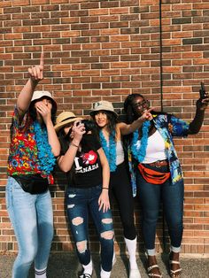 three women standing next to each other in front of a brick wall with one pointing at the camera