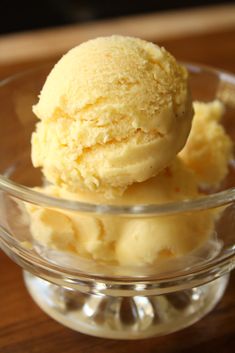 two scoops of ice cream sit in a glass bowl on a wooden table top